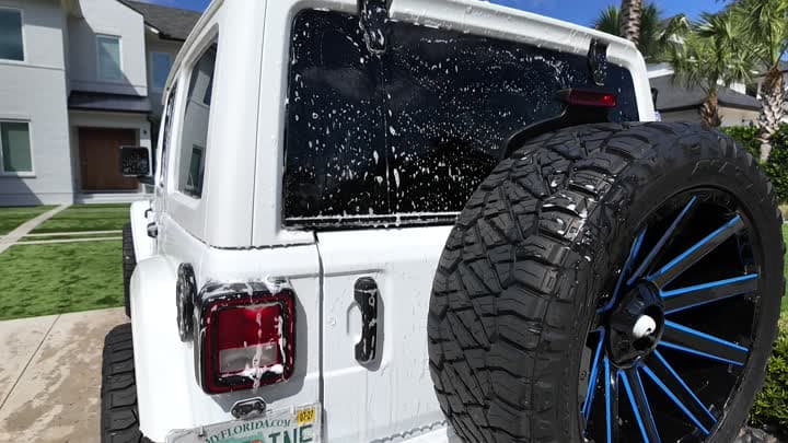 Soaped white Jeep Gladiator with a teal spare wheel under the carport